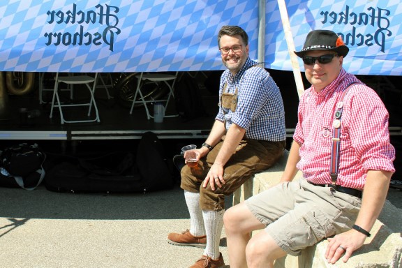 Two men in German garb smile, sitting behind the tent.